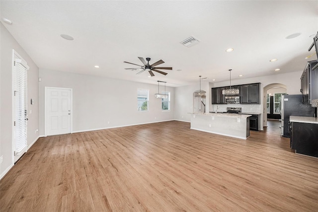 unfurnished living room featuring light wood finished floors, visible vents, arched walkways, a ceiling fan, and recessed lighting