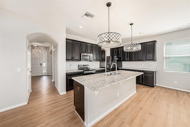 kitchen featuring arched walkways, a sink, visible vents, appliances with stainless steel finishes, and a center island with sink