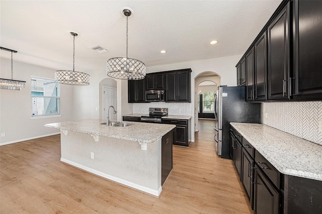 kitchen featuring a sink, appliances with stainless steel finishes, arched walkways, and dark cabinetry