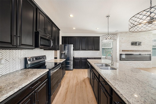 kitchen with stainless steel appliances, a sink, dark cabinetry, light wood finished floors, and pendant lighting