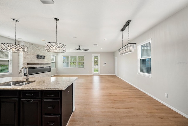 kitchen with light stone counters, open floor plan, hanging light fixtures, light wood-style floors, and a sink