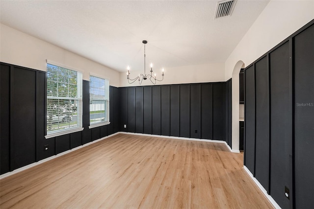 unfurnished room featuring light wood-style floors, visible vents, arched walkways, and a notable chandelier