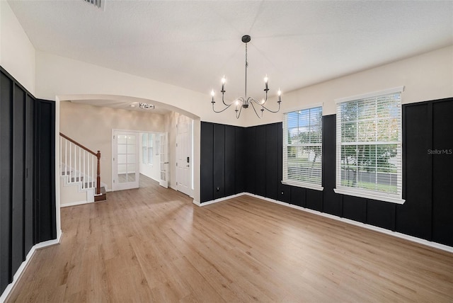 empty room with arched walkways, baseboards, light wood-style flooring, an inviting chandelier, and stairs