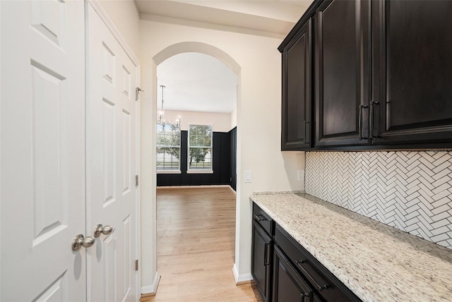 kitchen with arched walkways, baseboards, light stone countertops, light wood finished floors, and tasteful backsplash