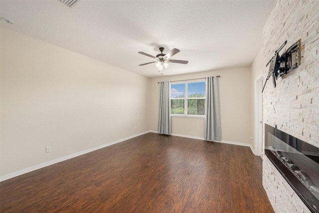 unfurnished living room with baseboards, ceiling fan, dark wood-style flooring, a textured ceiling, and a stone fireplace