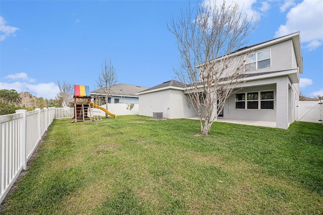 rear view of property with a playground, stucco siding, a lawn, central AC, and a fenced backyard