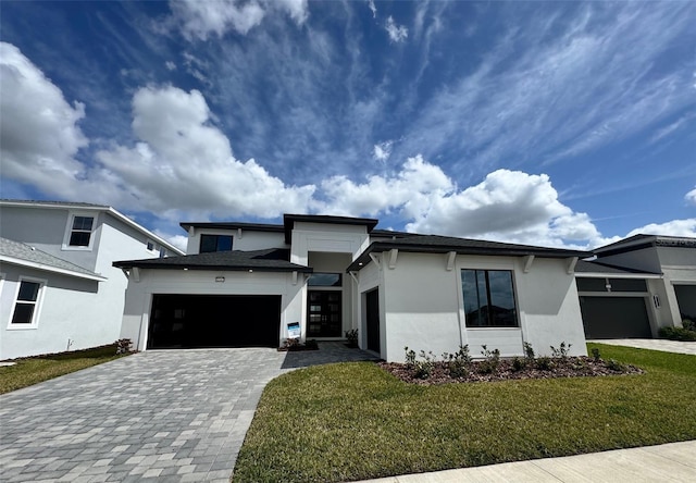 view of front of home with a front yard, decorative driveway, an attached garage, and stucco siding