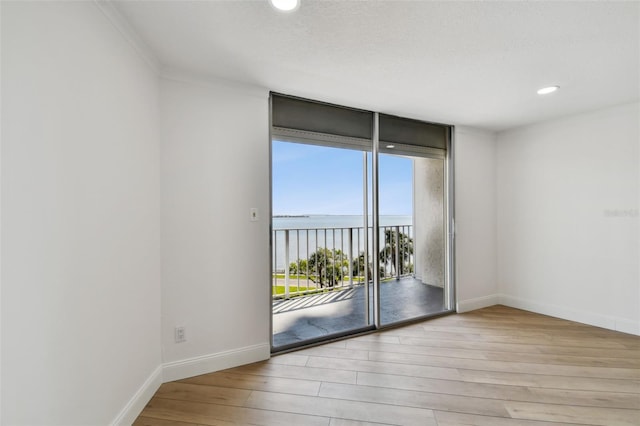 spare room with recessed lighting, a wall of windows, baseboards, and wood finished floors