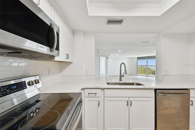 kitchen with visible vents, light stone countertops, white cabinets, stainless steel appliances, and a sink