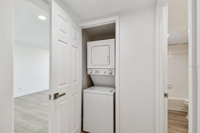 washroom featuring laundry area, baseboards, light wood-style floors, and stacked washer and dryer