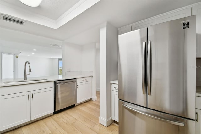 kitchen with visible vents, a sink, appliances with stainless steel finishes, light wood finished floors, and light countertops