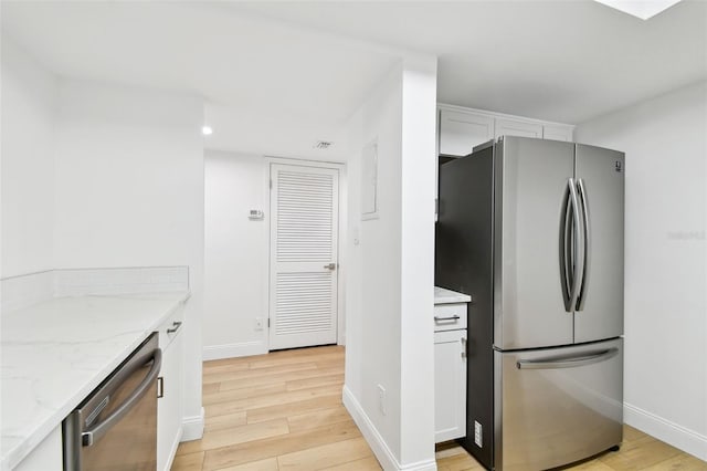 kitchen with white cabinets, light stone counters, light wood-style floors, and stainless steel appliances