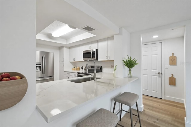 kitchen with visible vents, a kitchen bar, light wood-style flooring, appliances with stainless steel finishes, and white cabinetry