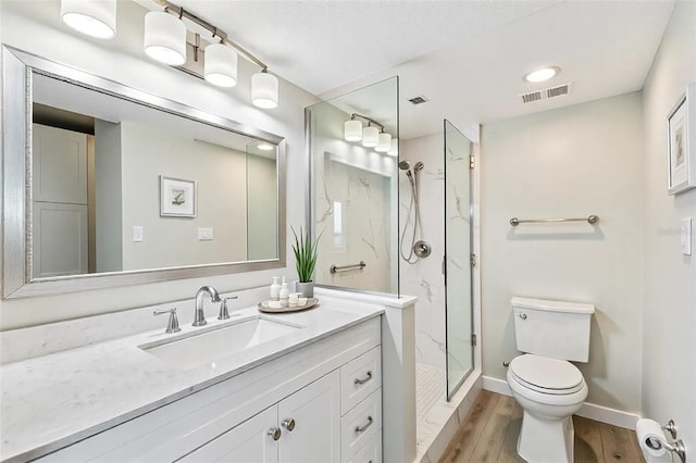 bathroom featuring visible vents, toilet, wood finished floors, a marble finish shower, and vanity
