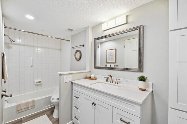 full bath featuring visible vents, toilet, vanity, wood finished floors, and a textured ceiling
