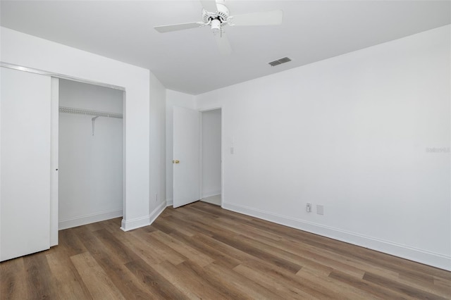 unfurnished bedroom with a closet, visible vents, ceiling fan, wood finished floors, and baseboards