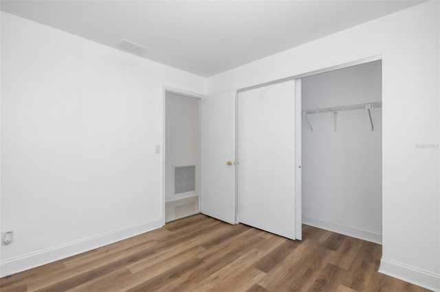 unfurnished bedroom featuring baseboards, a closet, visible vents, and wood finished floors