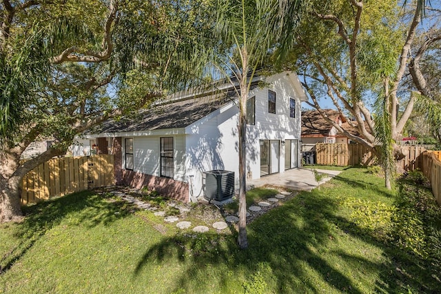 view of side of property featuring brick siding, a lawn, a patio area, cooling unit, and a fenced backyard