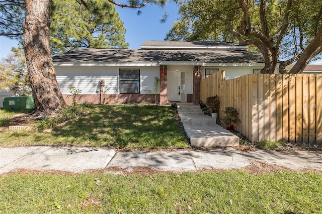 view of front of home featuring brick siding, fence, and a front lawn