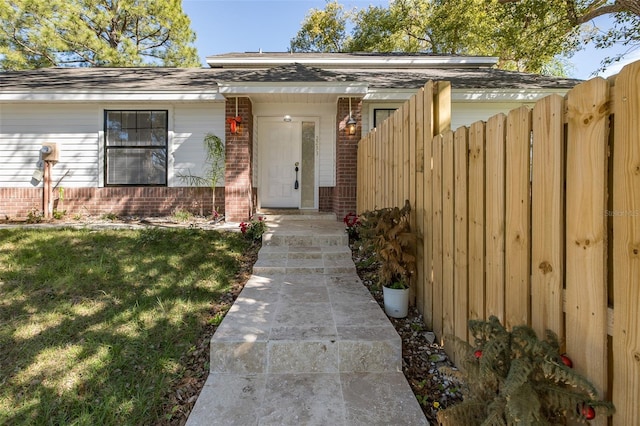 view of exterior entry featuring brick siding, a lawn, and fence