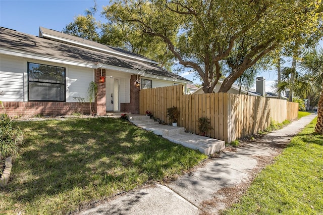 view of front facade with a front yard, brick siding, and fence