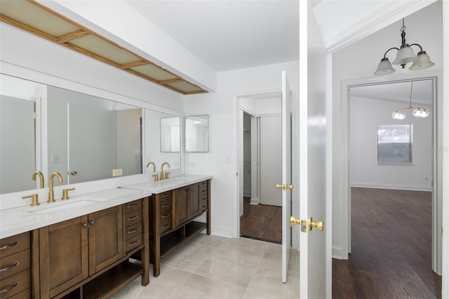 full bath with an inviting chandelier, a sink, baseboards, and double vanity