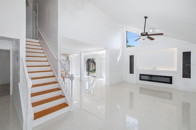 interior space with stairs, high vaulted ceiling, ceiling fan, and a glass covered fireplace