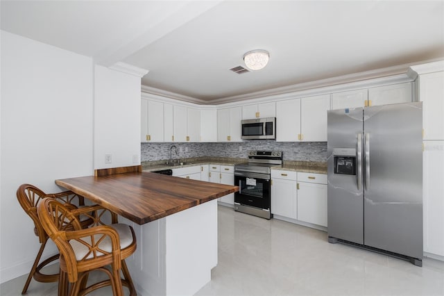 kitchen featuring stainless steel appliances, a peninsula, wood counters, visible vents, and decorative backsplash