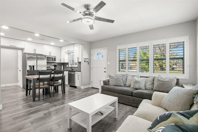 living area featuring recessed lighting, a ceiling fan, baseboards, and light wood finished floors