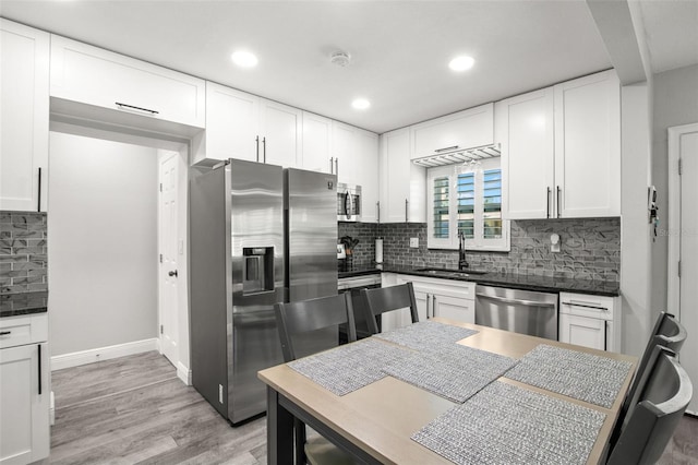 kitchen featuring dark countertops, appliances with stainless steel finishes, light wood-style floors, white cabinets, and a sink