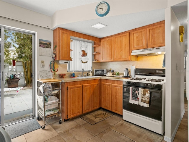 kitchen featuring gas range oven, light countertops, under cabinet range hood, open shelves, and a sink