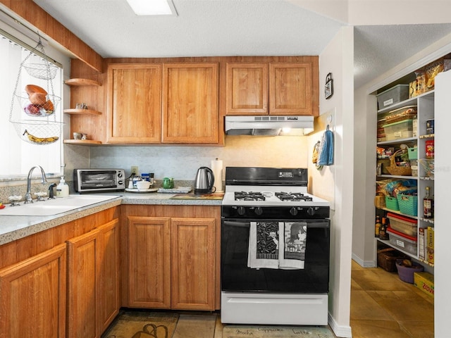 kitchen featuring light countertops, under cabinet range hood, open shelves, a sink, and gas stove