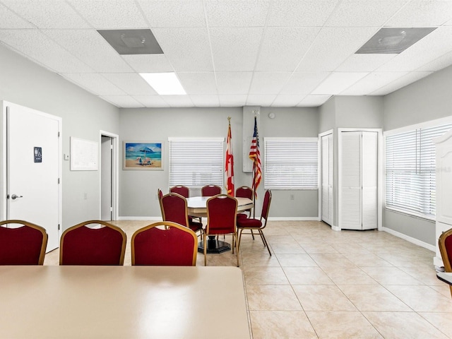 dining room with light tile patterned floors, a drop ceiling, and baseboards