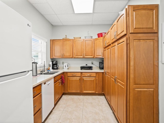 kitchen featuring white appliances, light tile patterned floors, a drop ceiling, light countertops, and a sink