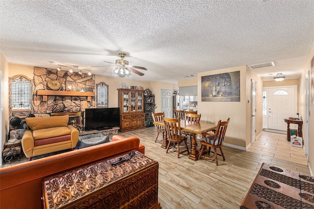 living area with a ceiling fan, light wood-type flooring, visible vents, and a textured ceiling