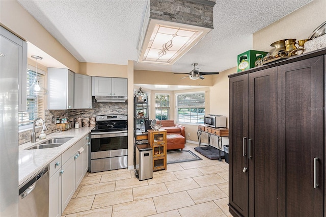 kitchen featuring tasteful backsplash, stainless steel appliances, under cabinet range hood, a sink, and light tile patterned flooring