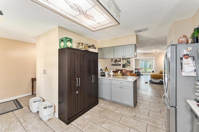 kitchen with visible vents, freestanding refrigerator, light countertops, a textured ceiling, and light tile patterned flooring