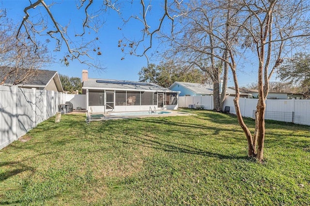 rear view of house with a chimney, a sunroom, a fenced backyard, and roof mounted solar panels