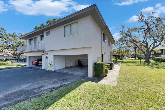 view of side of home with aphalt driveway, cooling unit, a garage, a yard, and stucco siding