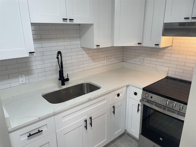 kitchen featuring tasteful backsplash, stainless steel electric range oven, white cabinetry, under cabinet range hood, and a sink