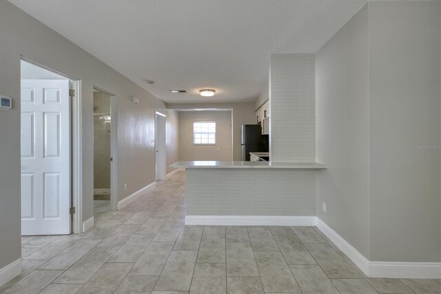 kitchen with freestanding refrigerator, a peninsula, light tile patterned flooring, light countertops, and baseboards
