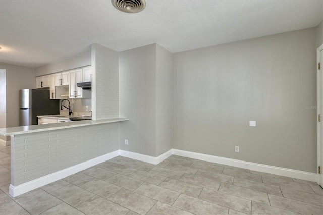 kitchen with baseboards, light countertops, freestanding refrigerator, white cabinetry, and visible vents