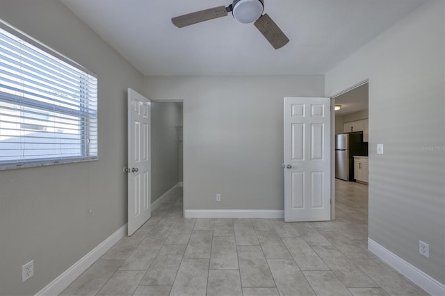 unfurnished bedroom with baseboards, a spacious closet, freestanding refrigerator, a ceiling fan, and light tile patterned flooring