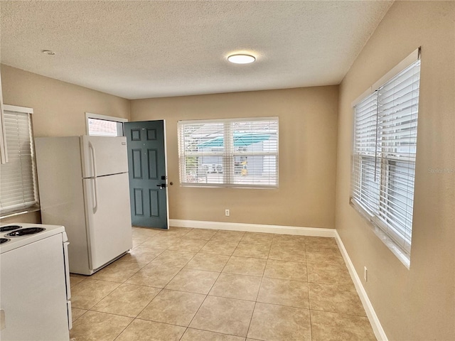 kitchen featuring a textured ceiling, light tile patterned floors, baseboards, and white appliances