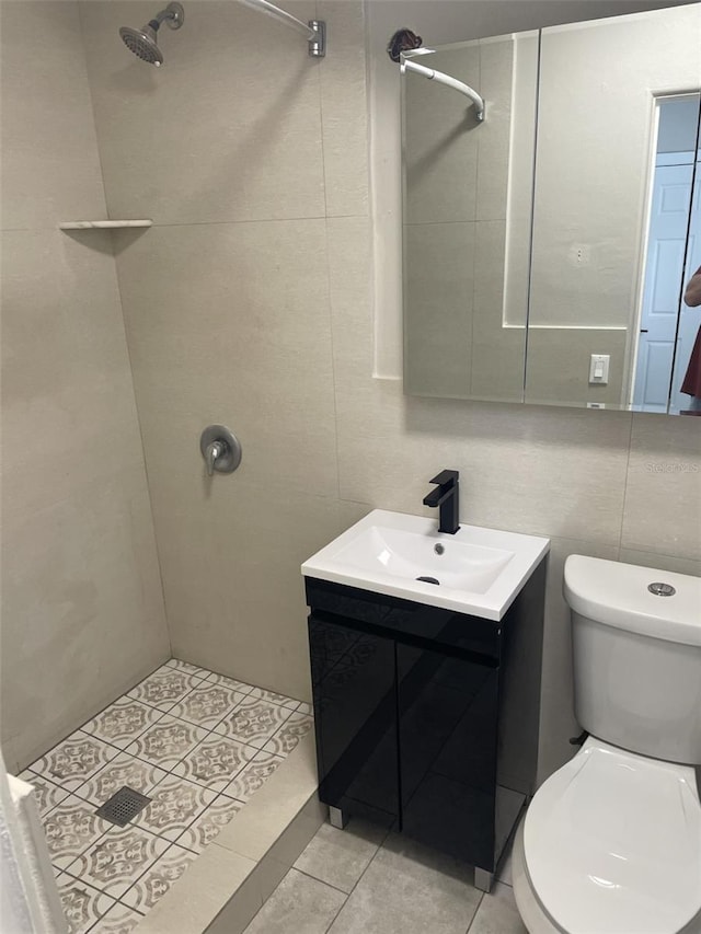 full bathroom featuring tiled shower, vanity, tile patterned flooring, toilet, and tile walls