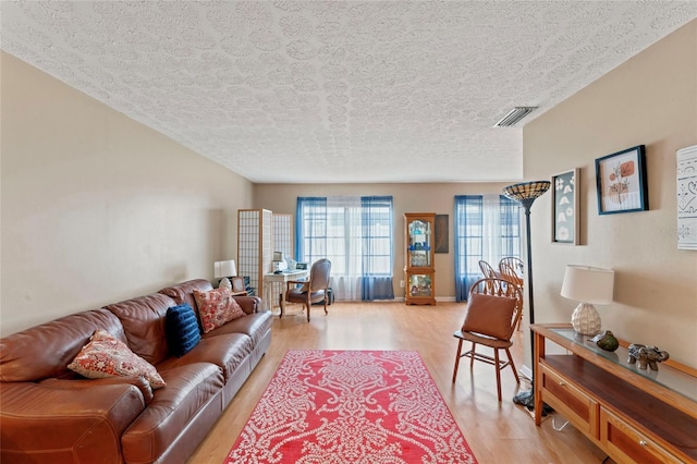 living area with a textured ceiling, light wood finished floors, and visible vents