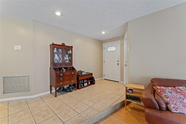 foyer entrance with a textured ceiling, light tile patterned flooring, visible vents, and baseboards