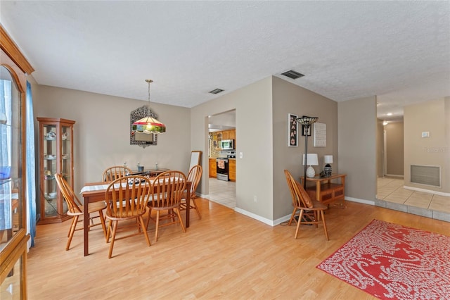 dining space featuring a textured ceiling, visible vents, and light wood-style floors