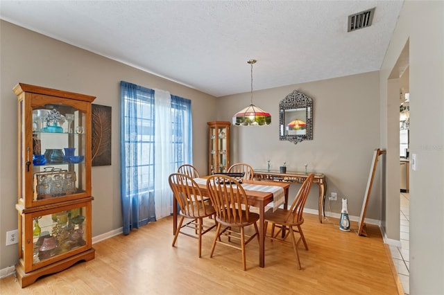 dining room with a textured ceiling, light wood-type flooring, visible vents, and baseboards