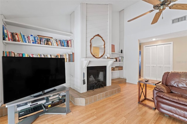 living area with visible vents, a fireplace with raised hearth, a ceiling fan, vaulted ceiling, and wood finished floors